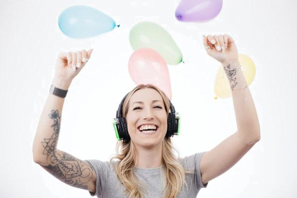 girl with headphones and hands up with balloons falling